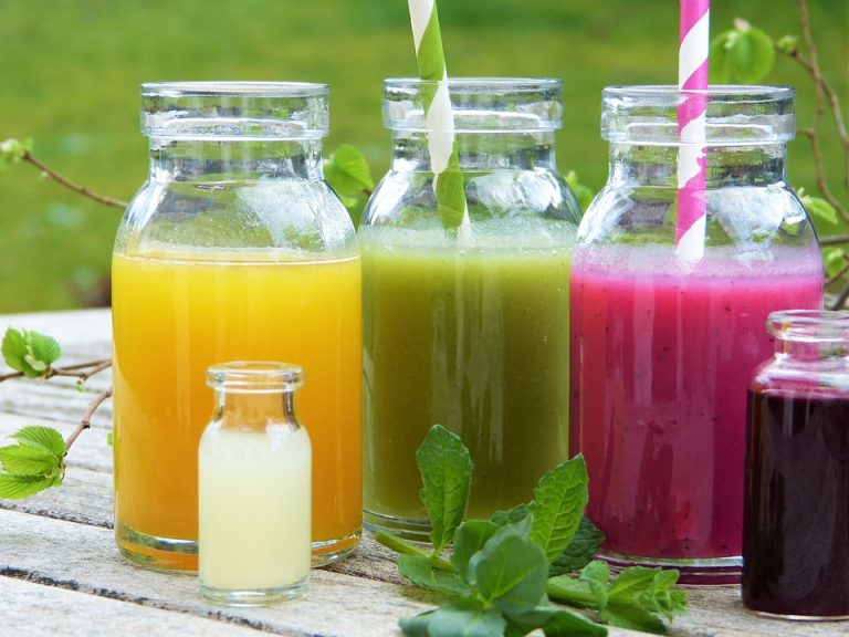 Colorful fruit juices in glass bottles with striped straws on a wooden table.