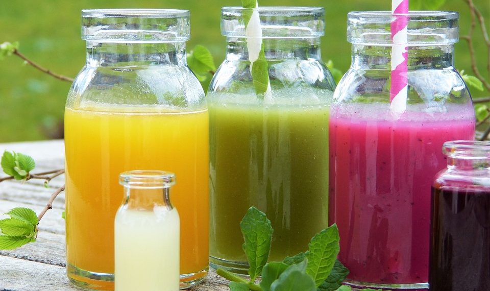 Colorful fruit juices in glass bottles with striped straws on a wooden table.