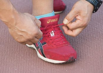 Tying red running shoe laces tightly on track.