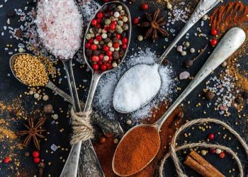 Various spices on spoons, including salt, pepper, mustard, and paprika.