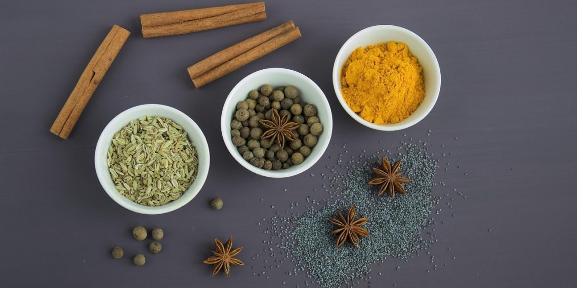 Bowls of spices including cinnamon, turmeric, and anise on a dark background.