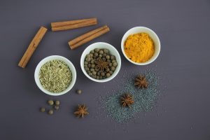 Bowls of spices including cinnamon, turmeric, and anise on a dark background.