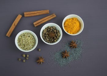 Bowls of spices including cinnamon, turmeric, and anise on a dark background.