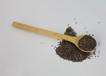 Wooden spoon with chia seeds scattered on a white background.