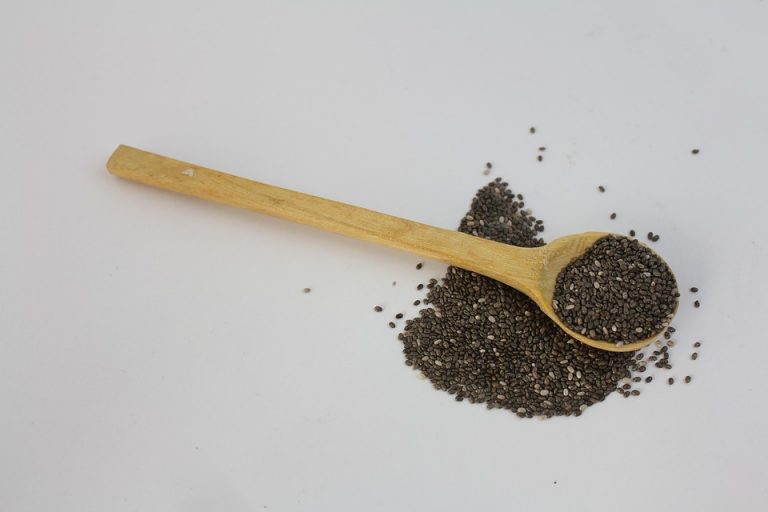 Wooden spoon with chia seeds scattered on a white background.