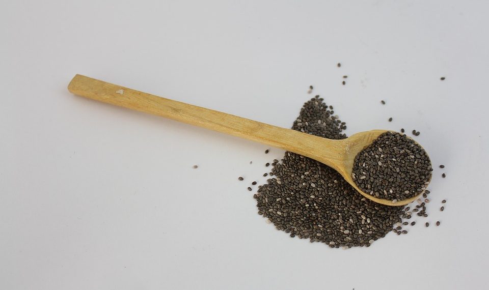Wooden spoon with chia seeds scattered on a white background.