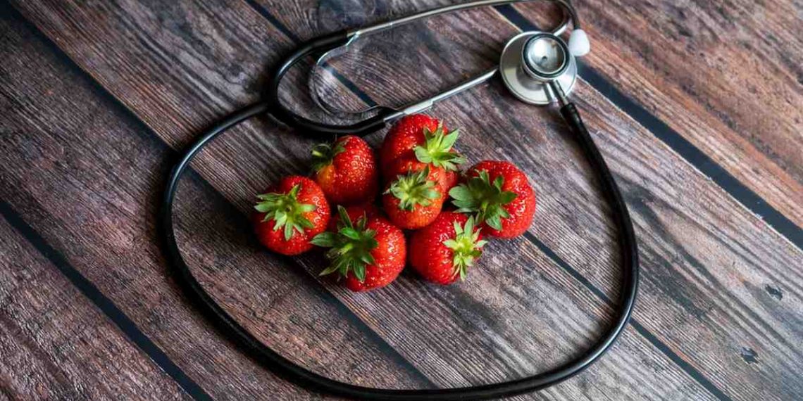 Stethoscope encircles fresh strawberries on wooden table.