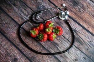 Stethoscope encircles fresh strawberries on wooden table.