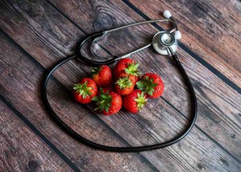 Stethoscope encircles fresh strawberries on wooden table.