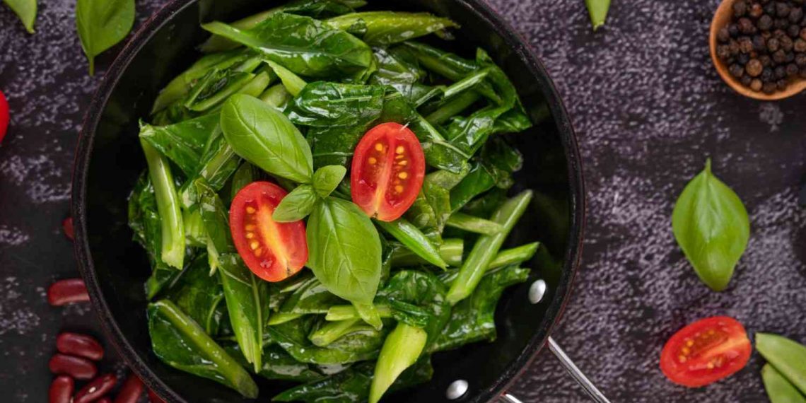 Stir-fried greens with tomatoes and basil in a pan.