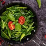 Stir-fried greens with tomatoes and basil in a pan.