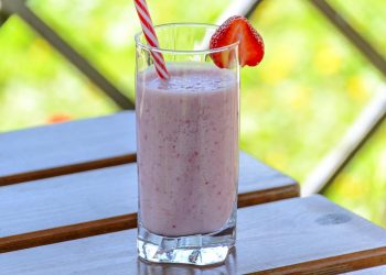 Strawberry smoothie in a glass with a straw on a table.
