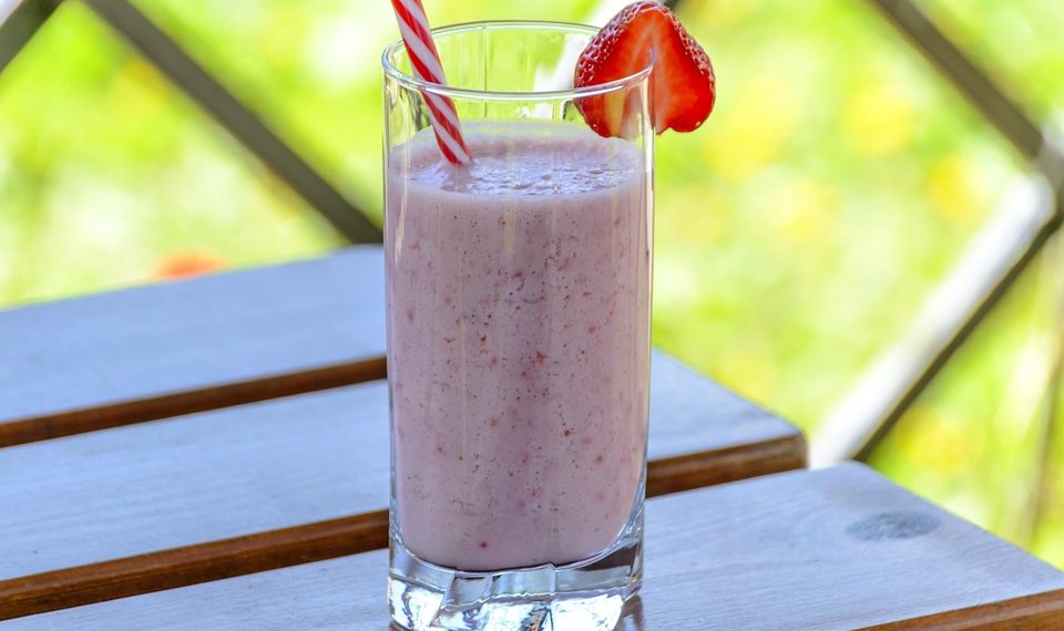 Strawberry smoothie in a glass with a straw on a table.