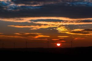 Wind turbines silhouetted against a vibrant sunset.
