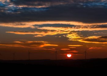 Wind turbines silhouetted against a vibrant sunset.