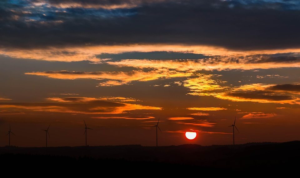 Wind turbines silhouetted against a vibrant sunset.