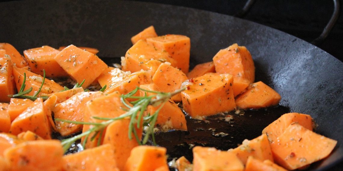 Cubed sweet potatoes roasting with rosemary and herbs in a pan.