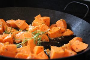 Cubed sweet potatoes roasting with rosemary and herbs in a pan.