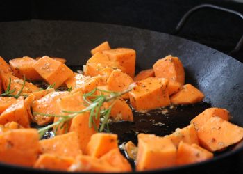 Cubed sweet potatoes roasting with rosemary and herbs in a pan.