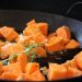 Cubed sweet potatoes roasting with rosemary and herbs in a pan.