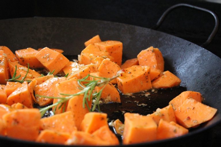 Cubed sweet potatoes roasting with rosemary and herbs in a pan.