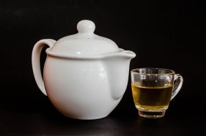White teapot with a glass cup of herbal tea.