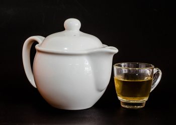 White teapot with a glass cup of herbal tea.