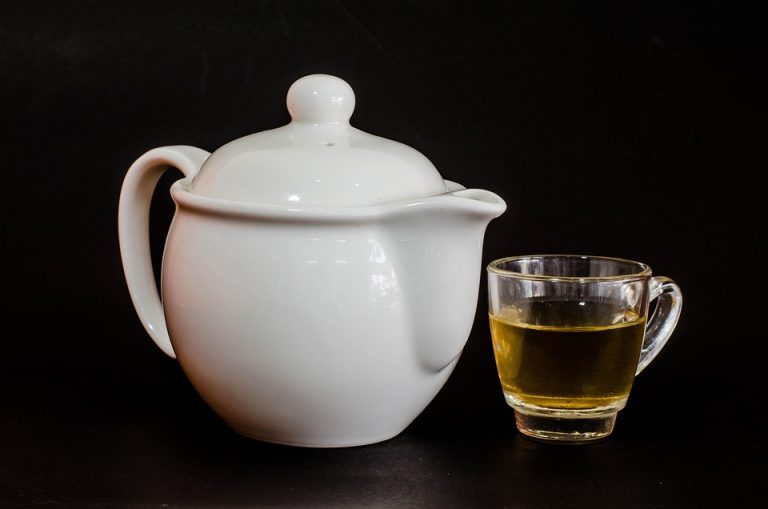 White teapot with a glass cup of herbal tea.