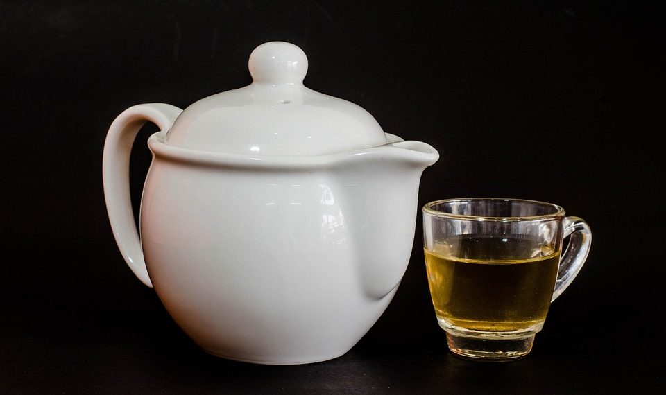 White teapot with a glass cup of herbal tea.