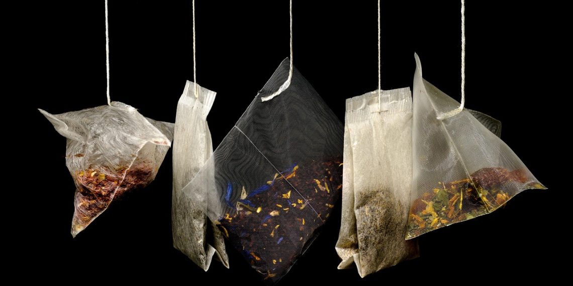 Mixed herbal tea bags hanging against a dark background.