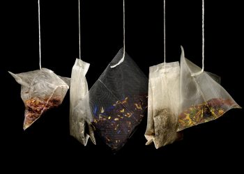 Mixed herbal tea bags hanging against a dark background.