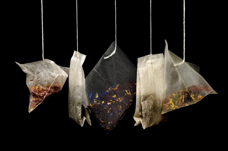 Mixed herbal tea bags hanging against a dark background.