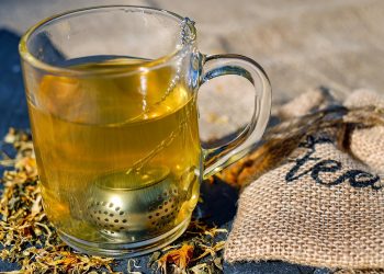 Glass of herbal tea with infuser next to burlap tea bag.