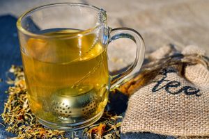 Glass of herbal tea with infuser and burlap tea bag.