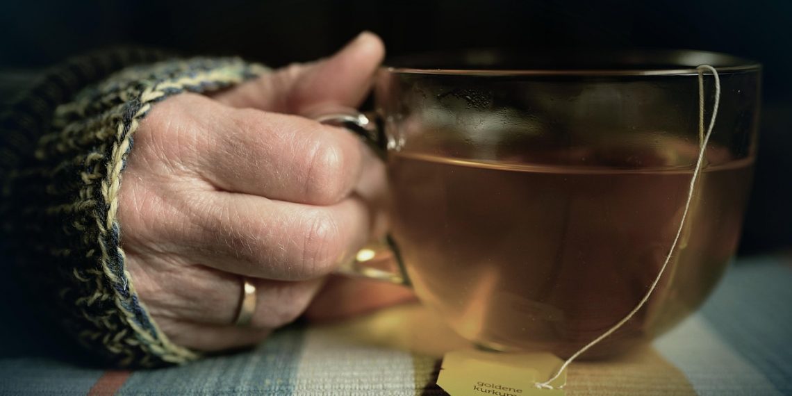 Hand holding a cup of herbal tea in a cozy setting.