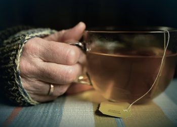 Hand holding a cup of herbal tea in a cozy setting.