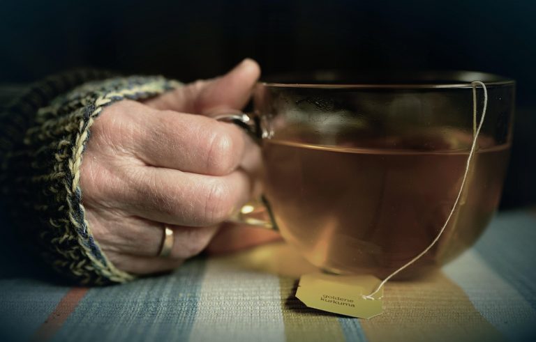 Hand holding a cup of herbal tea in a cozy setting.