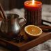 Cinnamon sticks and orange on tray with lit candle.