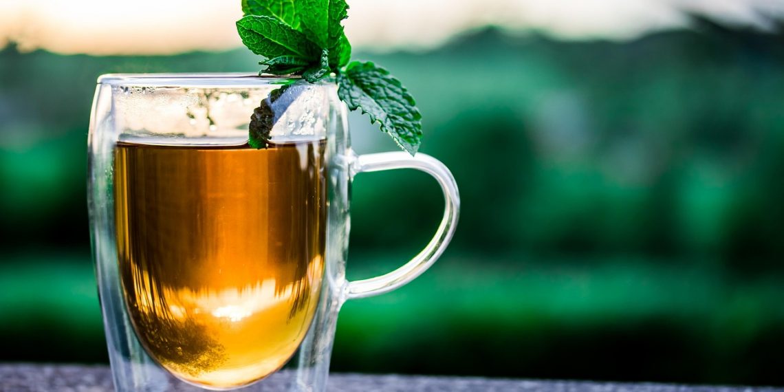 Tea with mint leaves in a clear glass on an outdoor table.