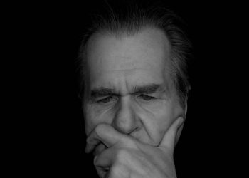 Elderly man deep in thought, contemplating in darkness.