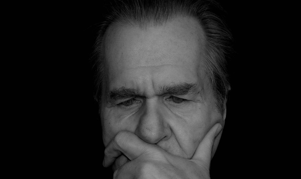 Elderly man deep in thought, contemplating in darkness.