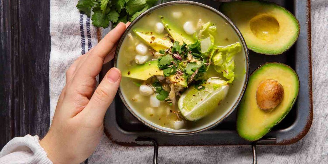 Green pozole with avocado and lime, garnished with cilantro.