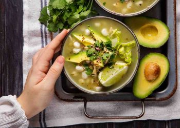 Green pozole with avocado and lime, garnished with cilantro.