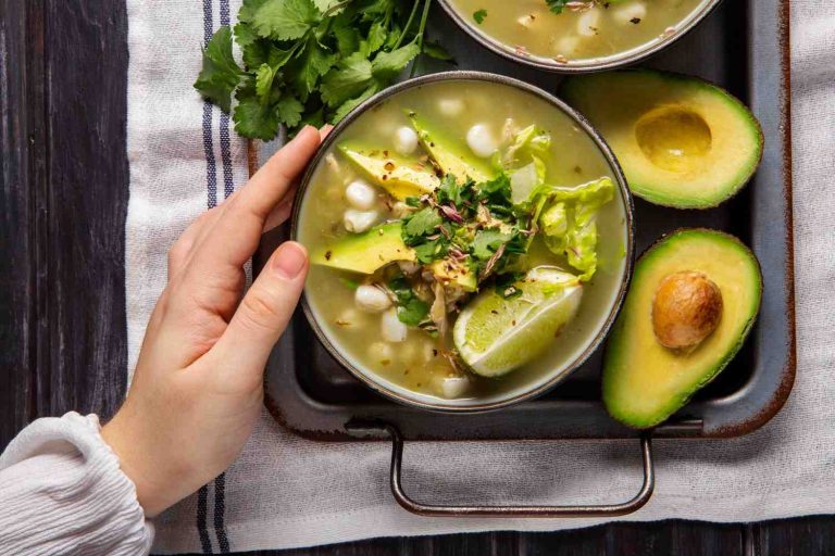 Green pozole with avocado and lime, garnished with cilantro.