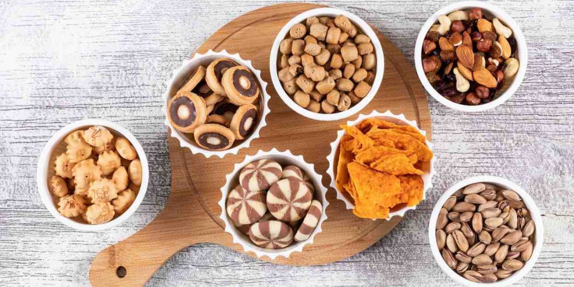 Assorted snacks in bowls on a wooden board.