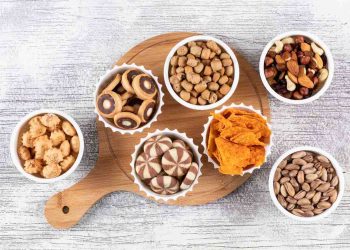Assorted snacks in bowls on a wooden board.