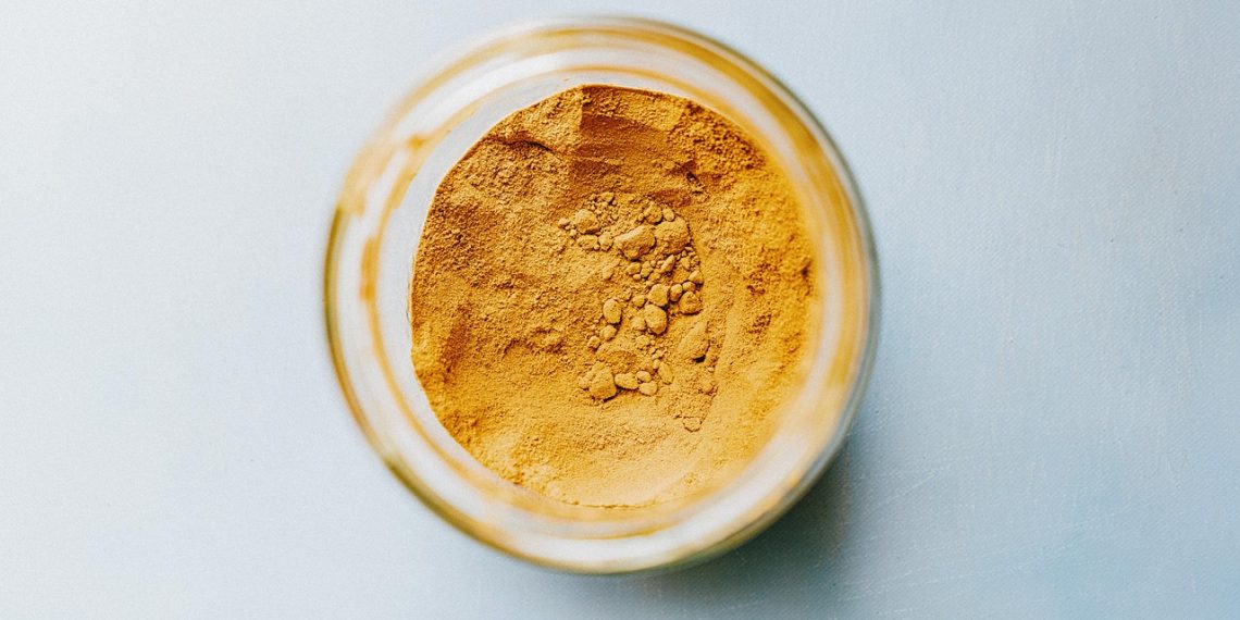 Jar filled with turmeric powder on a light blue surface.