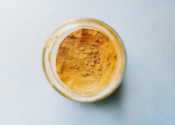 Jar filled with turmeric powder on a light blue surface.