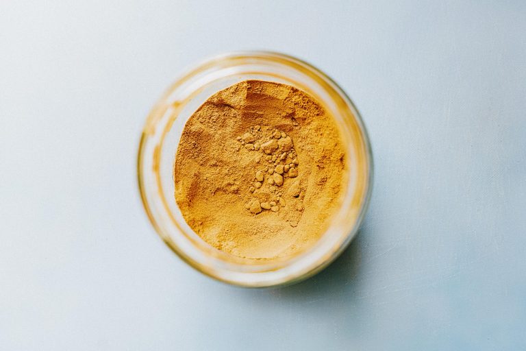 Jar filled with turmeric powder on a light blue surface.
