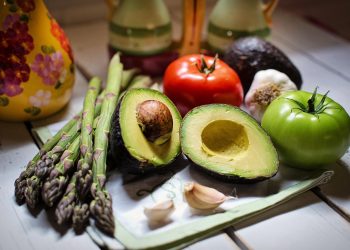 Fresh vegetables and avocado on a table with asparagus, tomato, and garlic.